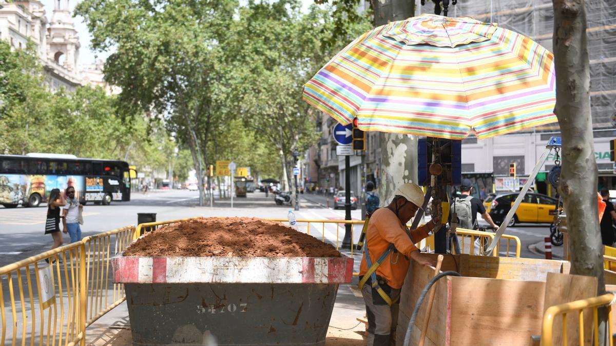 Un operario se protege del sol bajo una sombrilla en las obras de un colector en el cruce de Gran Vía con la calle de Balmes en Barcelona.