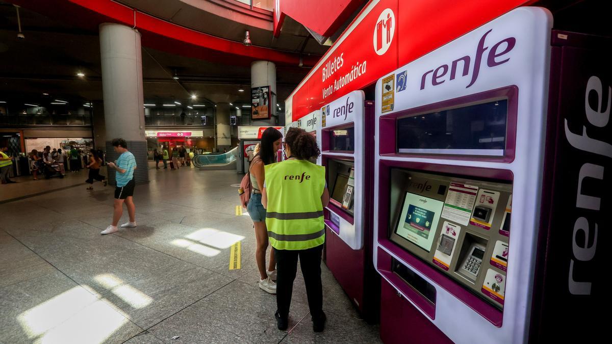 Una trabajadora de Renfe habla con una viajera delante de las máquinas expendedoras de billetes.