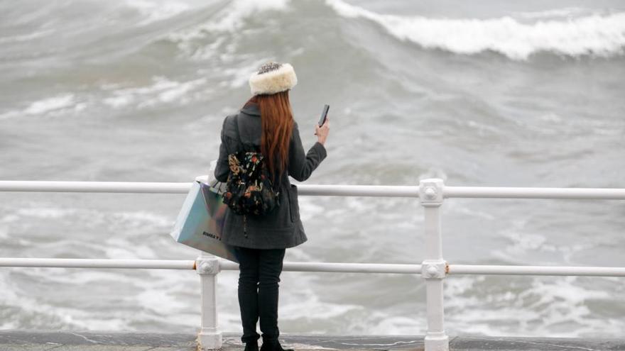 Una joven fotografía las olas en  Gijón