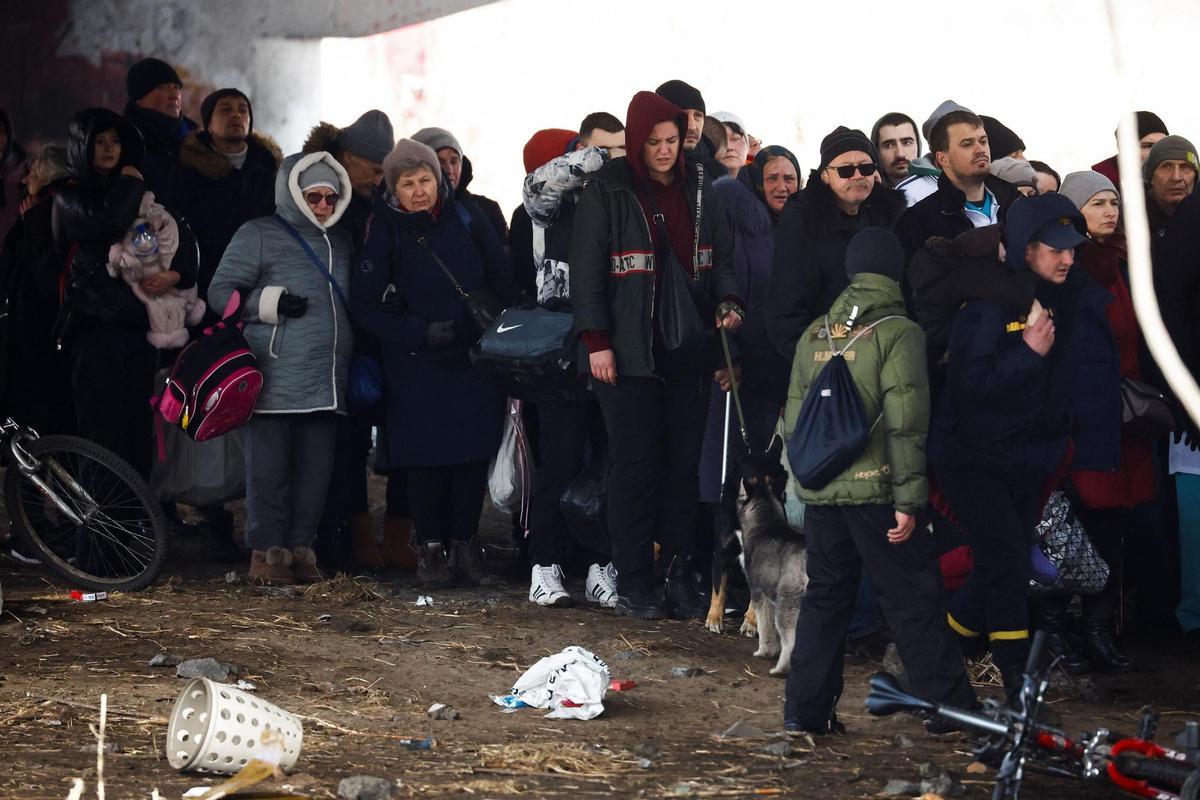 People wait below a destroyed bridge to cross a river as they flee from advancing Russian troops whose attack on Ukraine continues in the town of Irpin outside Kyiv