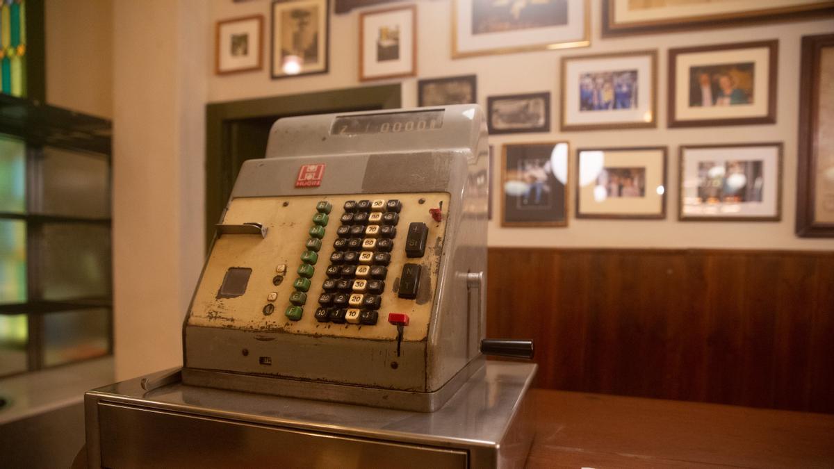 Una antigua mesa registradora que estaba en el altillo ahora se exhibe en la barra delante de recuerdos enmarcados.