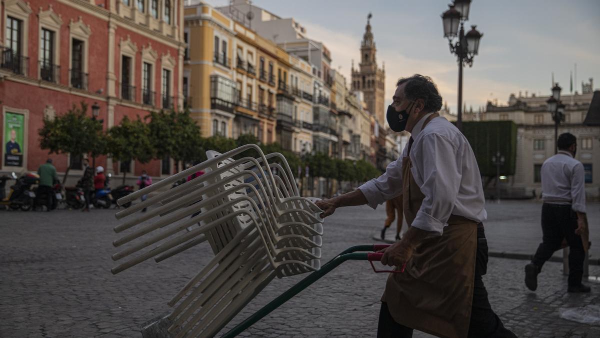 Un camarero recoge sillas de la terraza de un bar en Sevilla.
