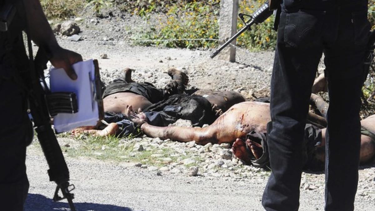 Police officers stand next to the dead bodies of eleven people lying on the side of a road in Chilapa
