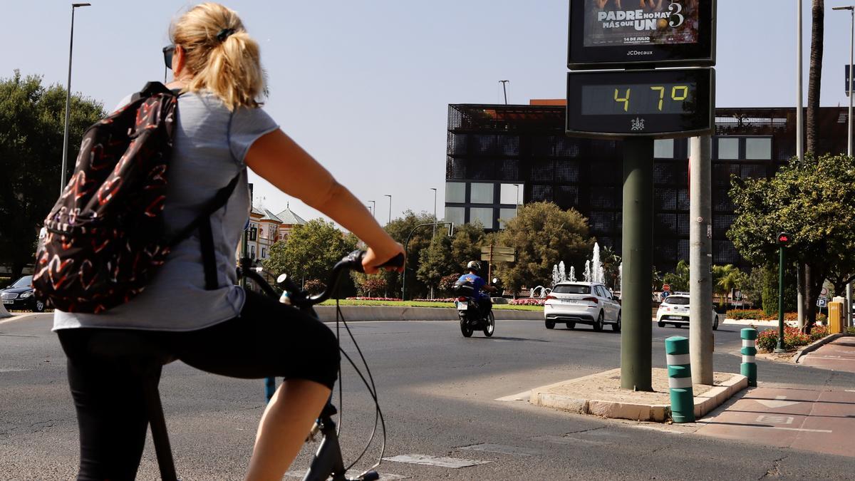 Una ciclista circula junto a un reloj que marca 47 grados al sol en Córdoba.