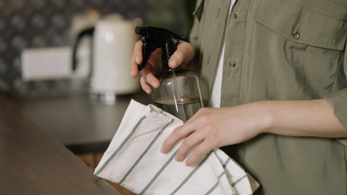 Una persona subjecta un drap i un recipient amb un producte de neteja a l'interior