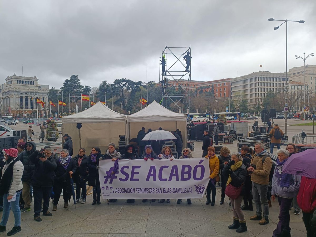 En primer plano, varias mujeres sujetan una pancarta con el lema 'Se acabó'. Al fondo, un grupo de operarios monta el escenario para la manifestación del sábdo contra la amnistía.