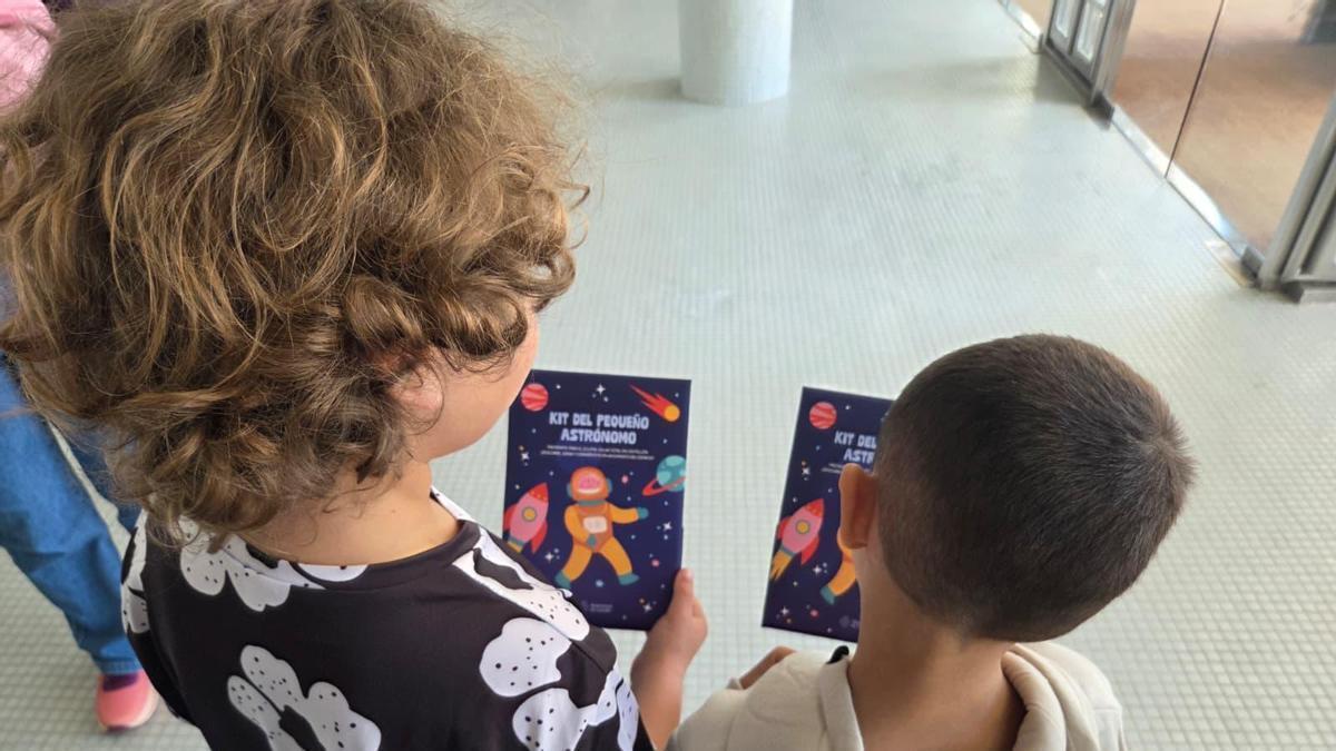 Unos niños miran un folleto del kit del pequeño astrónomo.