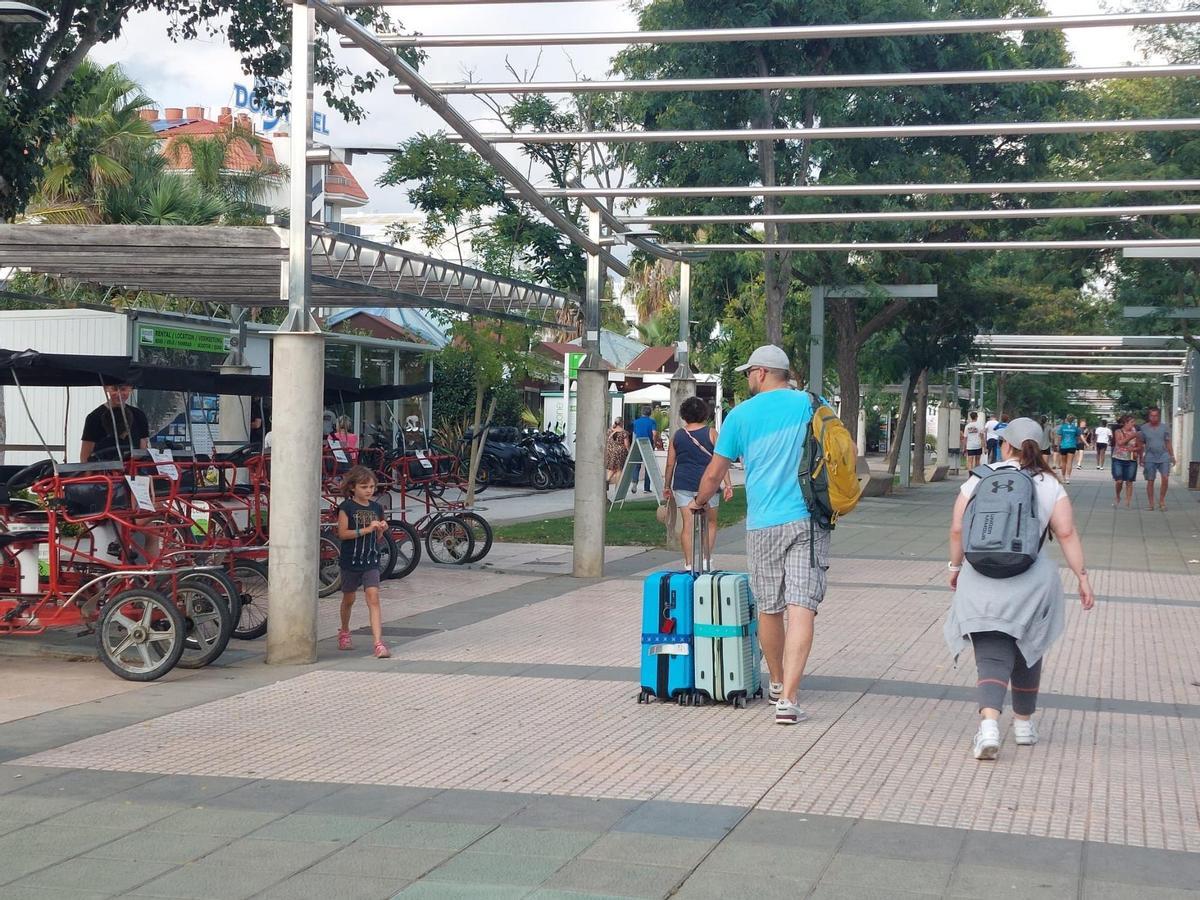 Turistas con maletas pasan junto a un tenderete de alquiler de bicicletas en Santa Susanna.