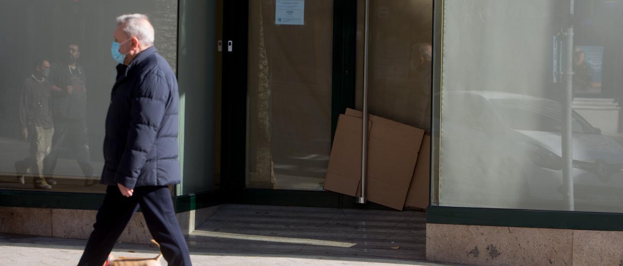 Un señor pasa junto a una sucursal bancaria cerrada en Alicante