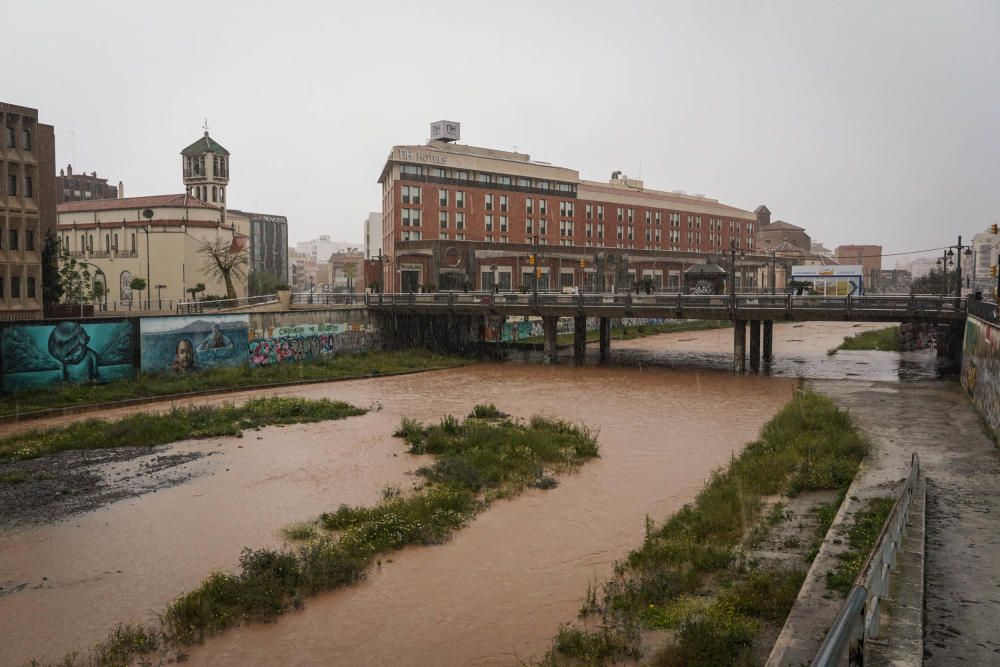 El río Guadalmedina crecido con agua y calles del Centro y el entorno del cauce, desiertas bajo la lluvia, la estampa de este martes 31 de marzo.