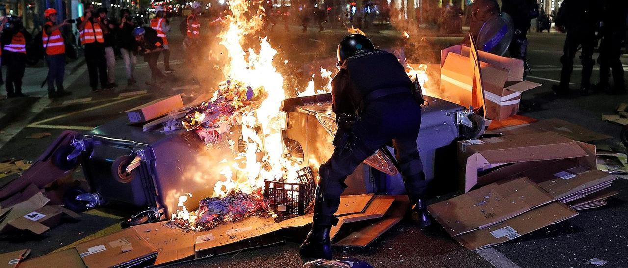 Un agente de los Mossos frente a unos contenedores ardiendo.