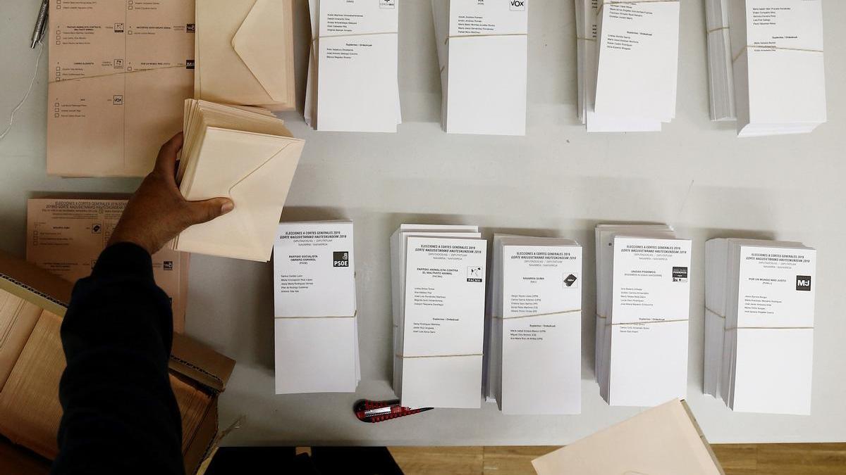 Una persona coloca en la mesa de un colegio electoral de Pamplona las papeletas con las diferentes opciones políticas, en 2019.