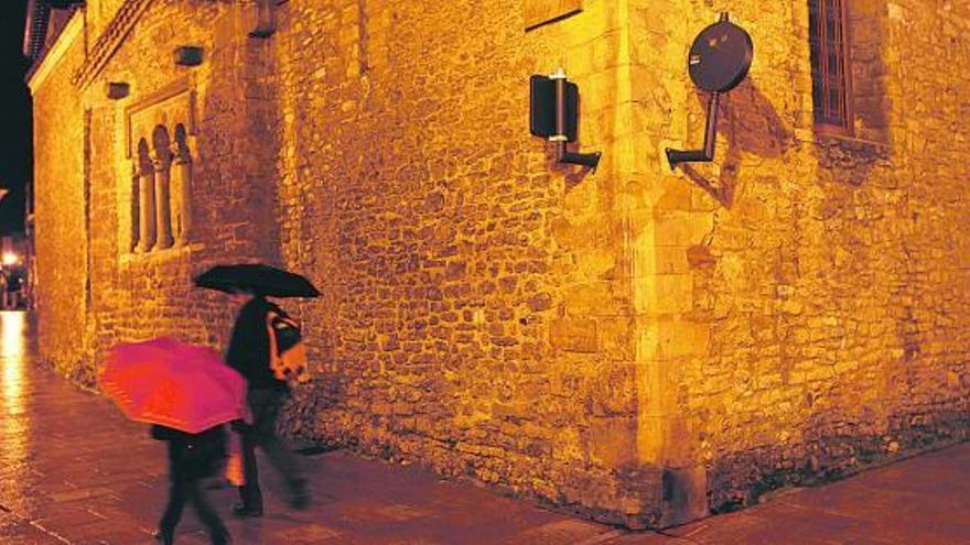Dos viandantes, ayer, pasan junto a San Tirso, en cuyo muro pueden verse las dos señales. / luisma murias