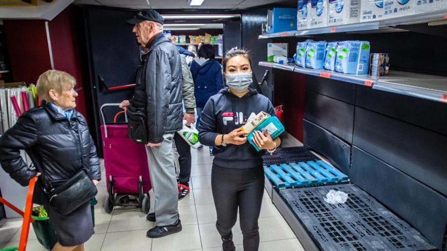 Una clienta con una mascarilla realiza la compra en un Mercadona con estanterías vacías.