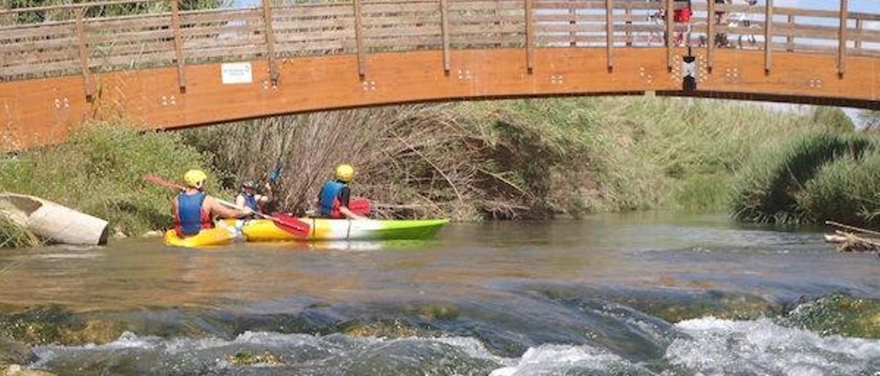 Dos excursionistas disfrutan del descenso en kayak. Sobre la pasarela, dos ciclistas.