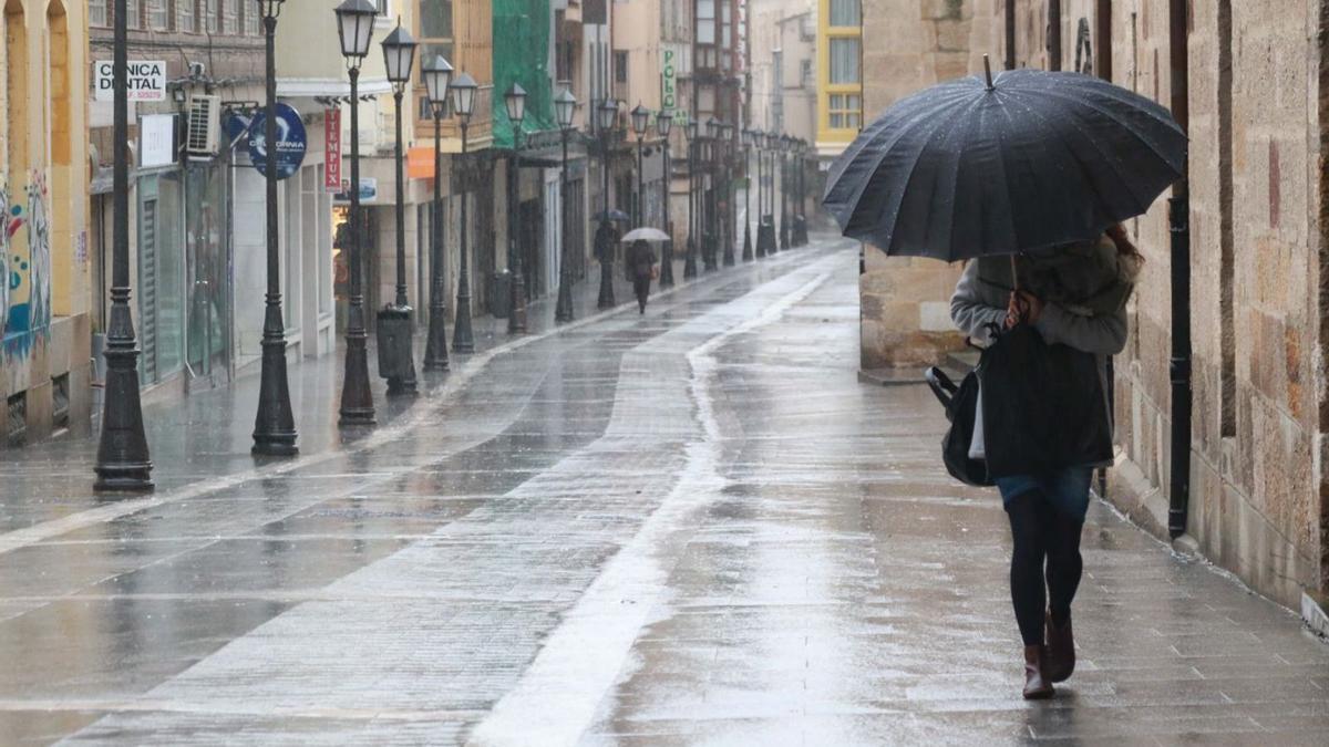 Una mujer se protege de la lluvia en la calle San Torcuato.
