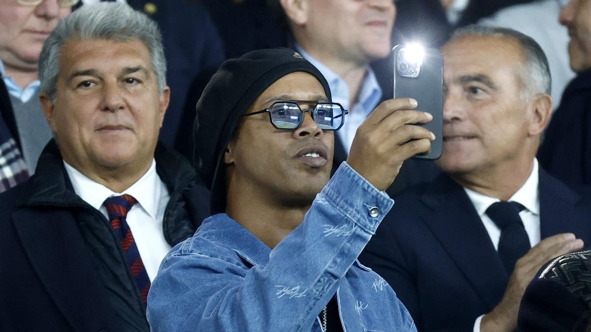Ronaldinho hace una foto del campo delante de Joan Laporta y Rafa Yuste, sentados en el palco.
