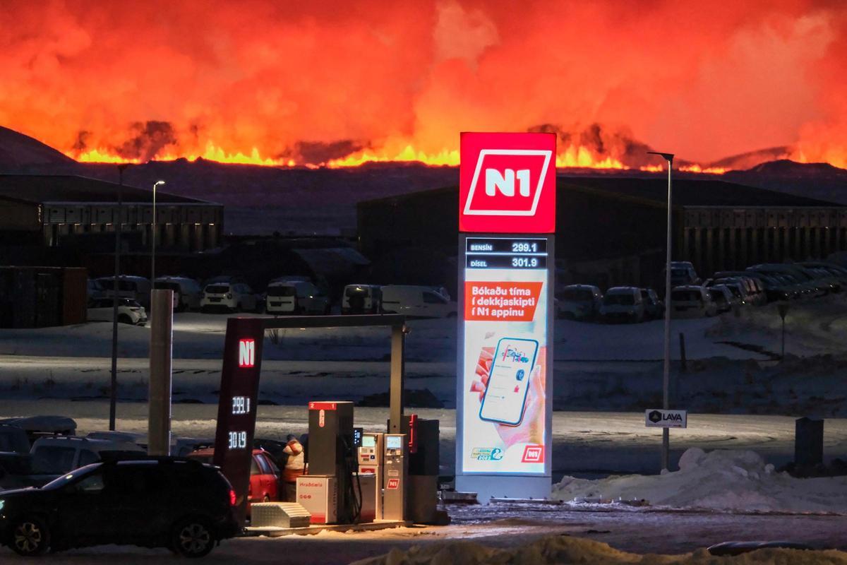 El logotipo de una gasolinera se ve mientras lava y nubes de humo salen de una fisura durante una erupción volcánica cerca de Grindavik, en el oeste de Islandia, el 8 de febrero de 2023.