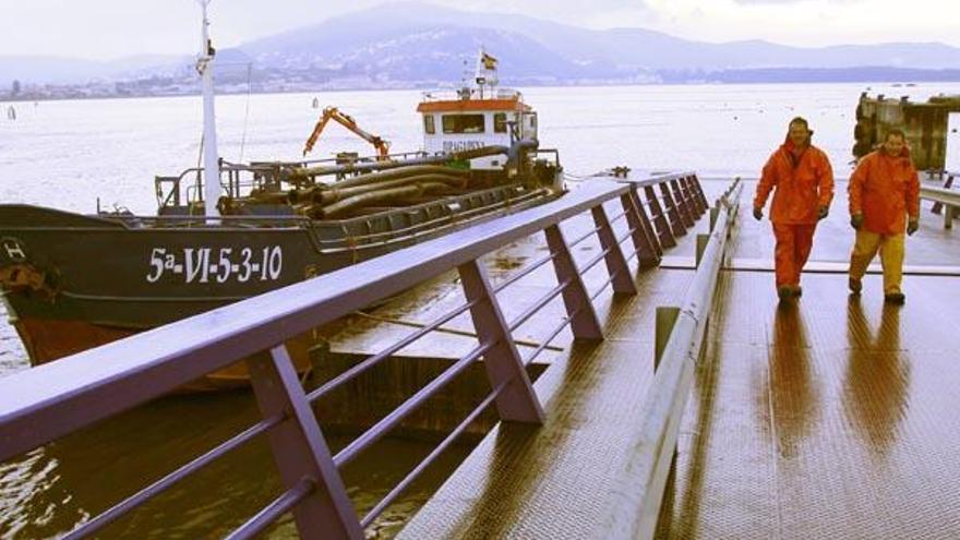 Dos operarios ayer junto al barco &quot;Dragarea&quot;, que extraerá la arena de la desembocadura del Miño.