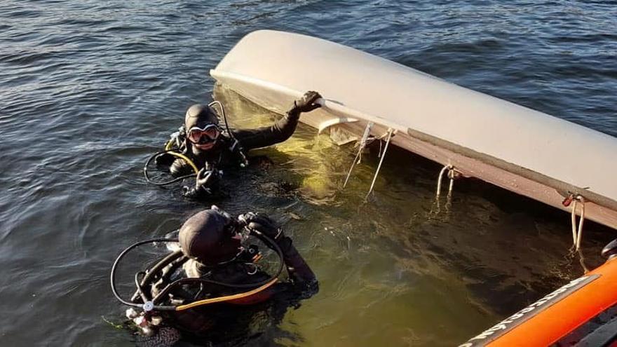 Miembros del equipo de rescate, con la embarcación volcada.