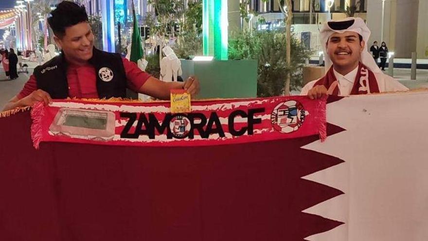 El seguidor rojiblanco posa con un qatarí, la bandera del país y la bufanda del Zamora CF en las calles de Doha.