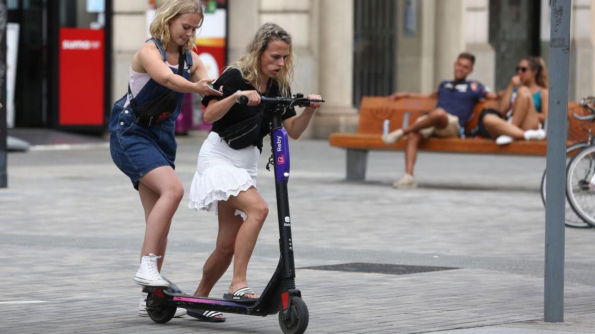 Dos jóvenes intentan subirse a un patinete compartido en Barcelona, en agosto de 2019, cuando las empresas operaban sin paraguas legal