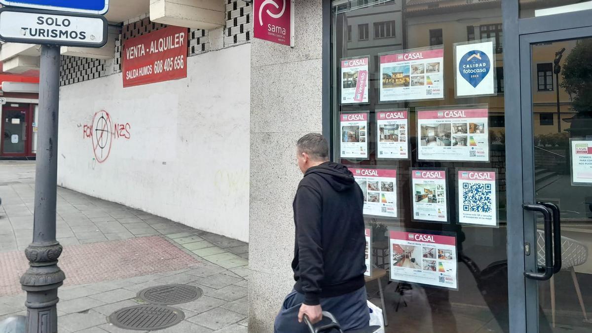 Un vecino pasa ante una inmobiliaria, con un anuncio del alquiler de un bajo comercial al fondo, en Langreo.