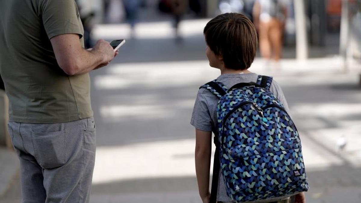 Un padre permanece atento a su móvil junto a su hijo, a la salida del colegio.