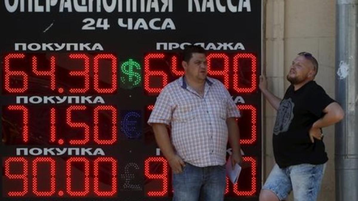 Dos hombres ante un panel que muestra el cambio del rublo en Moscú.
