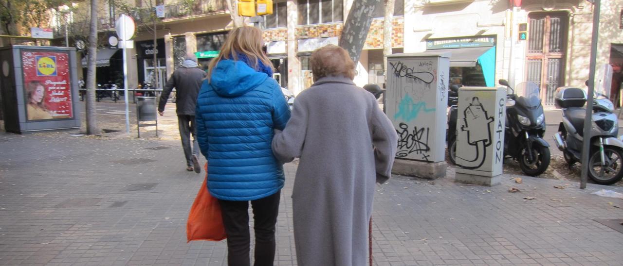 Una mujer acompaña por la calle a una persona mayor