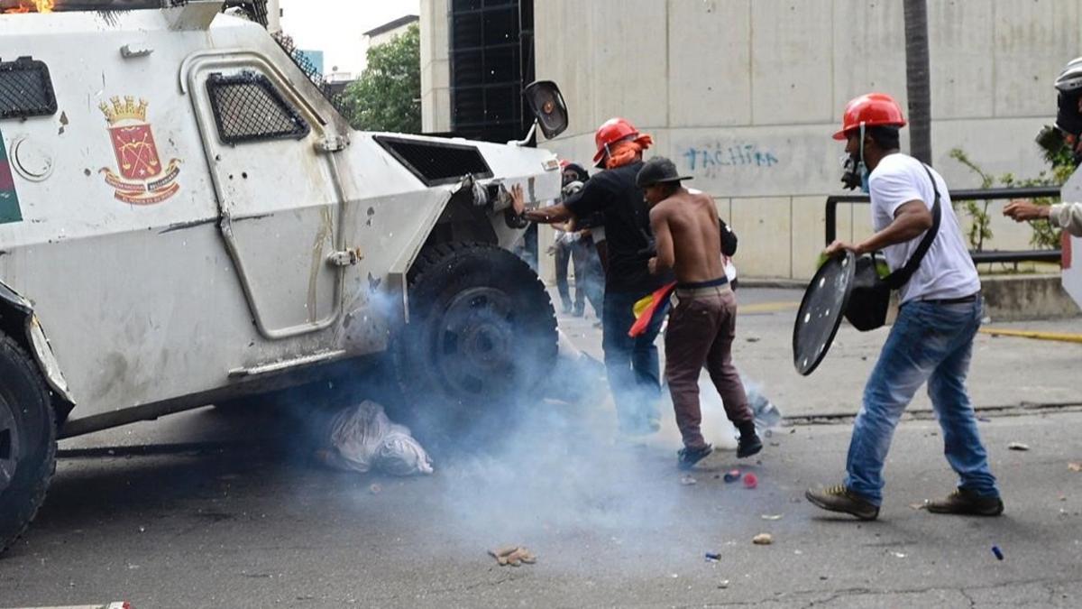 Un manifestante yace bajo una tanqueta policial en Caracas