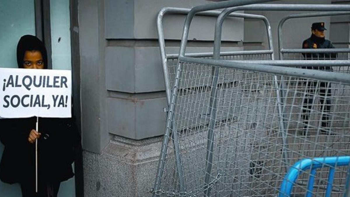 Una joven muestra un cartel reclamando el alquiler social en la concentración contra los desahucios que se celebró ayer en la calle que da acceso al Congreso de los Diputados.