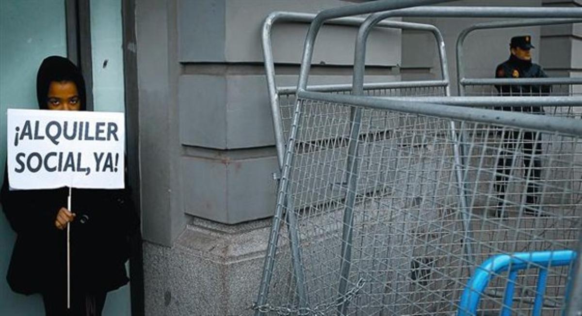 Una joven muestra un cartel reclamando el alquiler social en la concentración contra los desahucios que se celebró ayer en la calle que da acceso al Congreso de los Diputados.