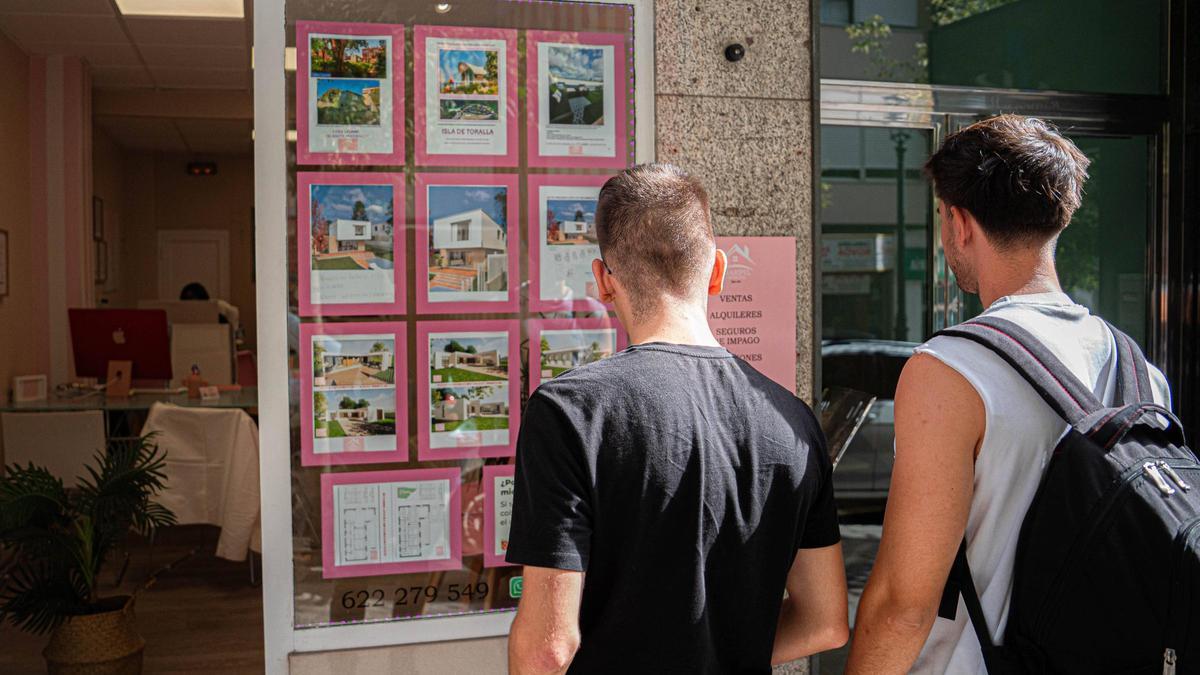 Dos jóvenes observan el escaparate de una inmobiliaria en Vigo.