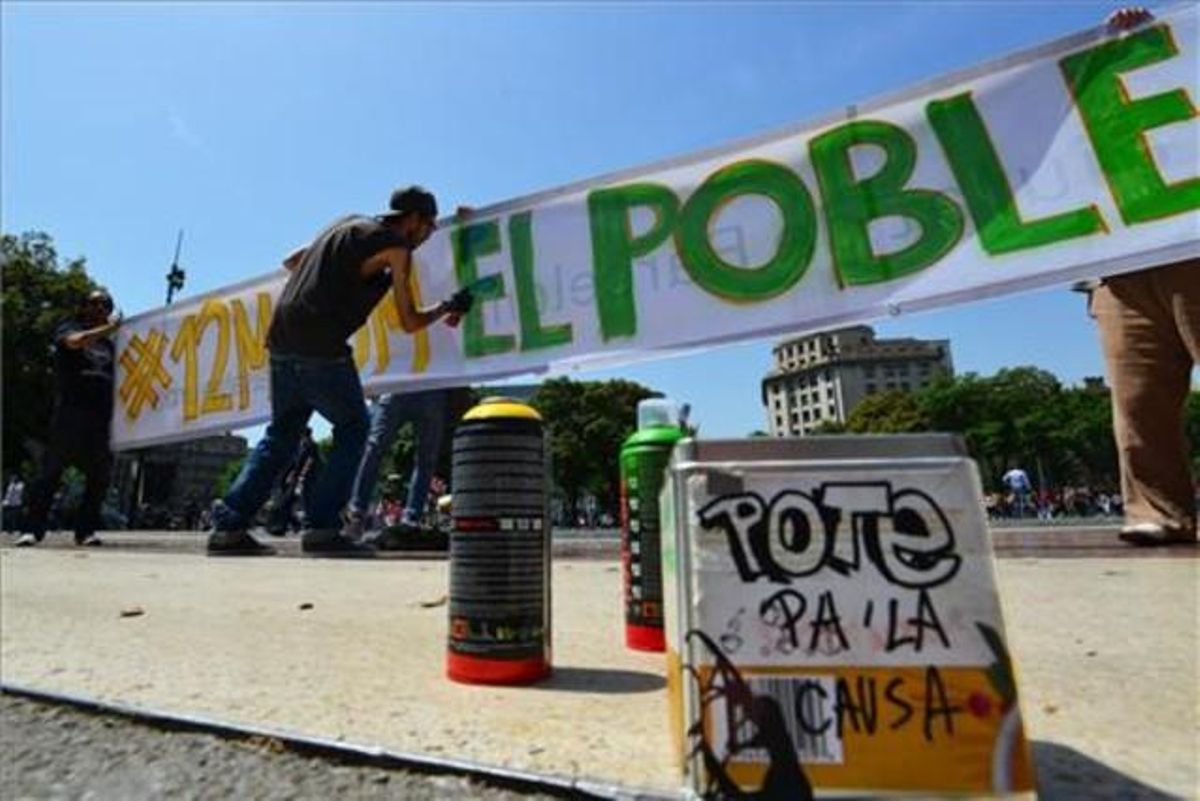 Integrants del moviment del 15-M ultimen la pancarta que encapçalarà la manifestació de Barcelona 12M-15M. El poble som la solució.