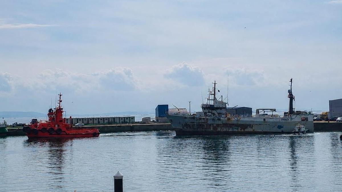 Un remolcador retirando el pesquero 'Awadi' que ardió en el puerto de Ribeira.
