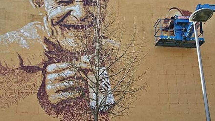 Rock BlackBock, penjat en un baló grua, pinta un dels rostres del seu mural.