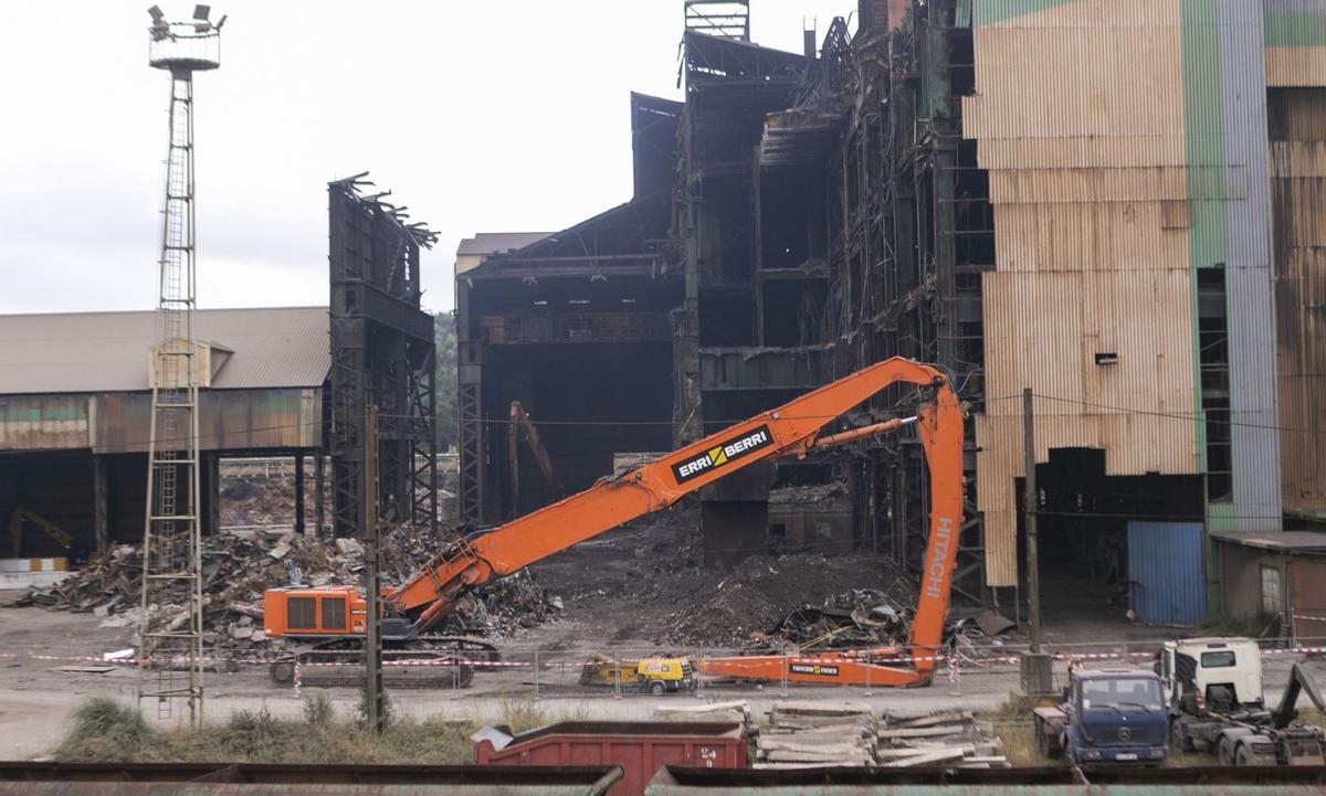 Una de las máquinas empleadas en el desmantelamiento de la acería, con el «mordisco» que ya se le ha dado al edificio en segundo término. | María Fuentes