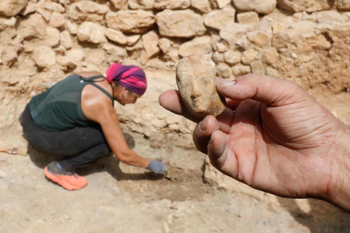 El rostre femení de trets arcaics en primer terme; al fons, una arqueòloga excavant la casa grega on s'ha trobat