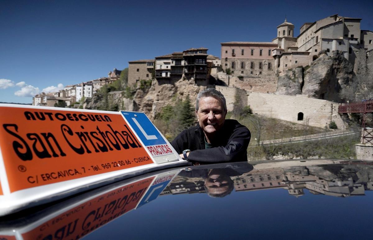 Rafael Lozano, propietario de la autoescuela San Cristóbal, posa junto a uno de sus coches frente a las casas colgadas de Cuenca.