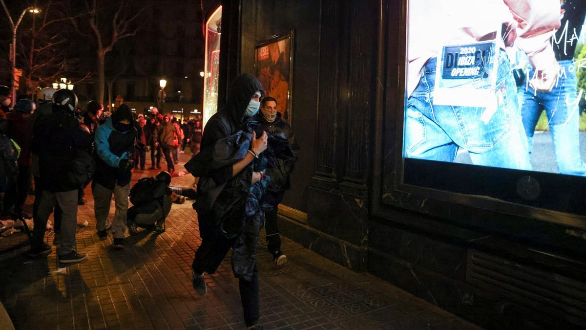 Un hombre sostiene ropa robada en una tienda, mientras los partidarios del rapero catalán arrestado Pablo Hasél protestan en Barcelona