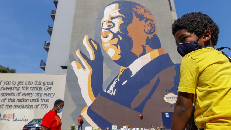 Un niño se sienta en los hombros de su padre mientras la gente se reúne en un gran mural de John Lewis.