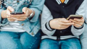 Dos adolescentes atentos a las pantallas de sus teléfonos móviles.