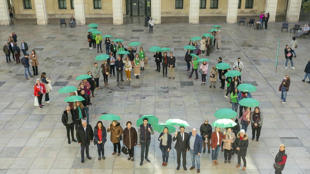 El lazo contra el cáncer formado con paraguas verdes en la plaza del Ayuntamiento de Alicante