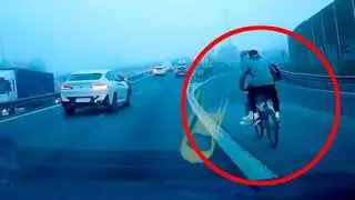 Imagen surrealista en la SE-30: un tipo con una bici y otro encaramado en la barra circulan en plena hora punta y con niebla