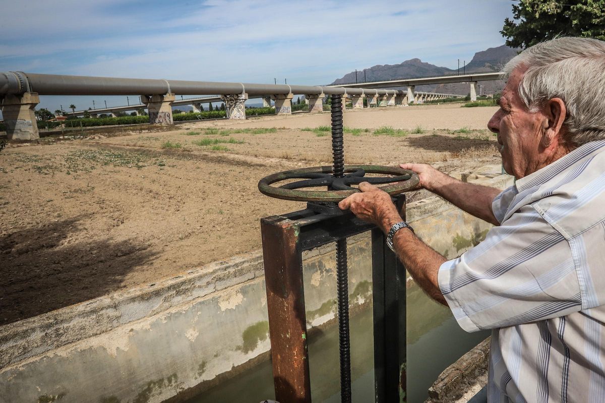 Un regante de la huerta tradicional abre una acequia. Al fondo el postrasvase Tajo-Segura entre Murcia y el embalse de La Pedrera