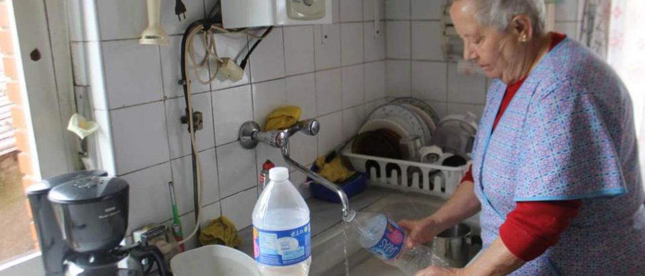 Alicia Alonso, ayer, recogiendo agua del grifo de su cocina en La Mortera (Candamo). A la derecha, Alberto García muestra el agua sucia en el lavabo.
