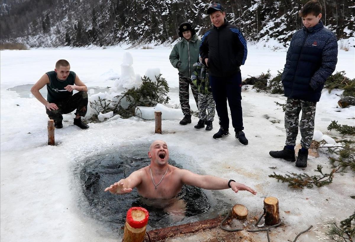 Los alumnos de un centro de rehabilitación para niños observan a su monitor Ilya Shelko darse un chapuzón en las frías aguas del río Mana cubierto de hielo en Siberia