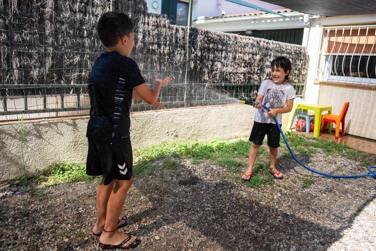 Dos hermanos se refrescan con una manguera en el patio de su casa.
