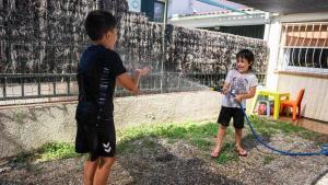 Dos hermanos se refrescan con una manguera en el patio de su casa.